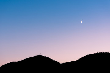 Crescent moon in sunset sky above sillhouette of mountains