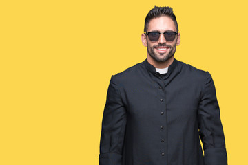 Young Christian priest wearing sunglasses over isolated background with a happy and cool smile on...