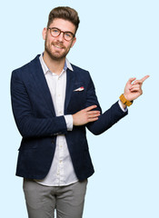 Young handsome business man wearing glasses with a big smile on face, pointing with hand and finger...