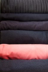 one bright thing coral color against the background of many black clothes in a neat stack