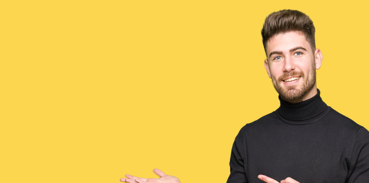 Young handsome blond man wearing winter sweater amazed and smiling to the camera while presenting with hand and pointing with finger.