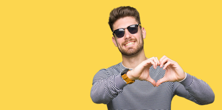 Young handsome man wearing sunglasses smiling in love showing heart symbol and shape with hands. Romantic concept.