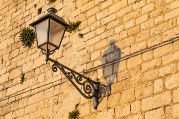 Italy, Apulia, Metropolitan City of Bari, Bari. Wrought-iron street lamp in a stone wall.