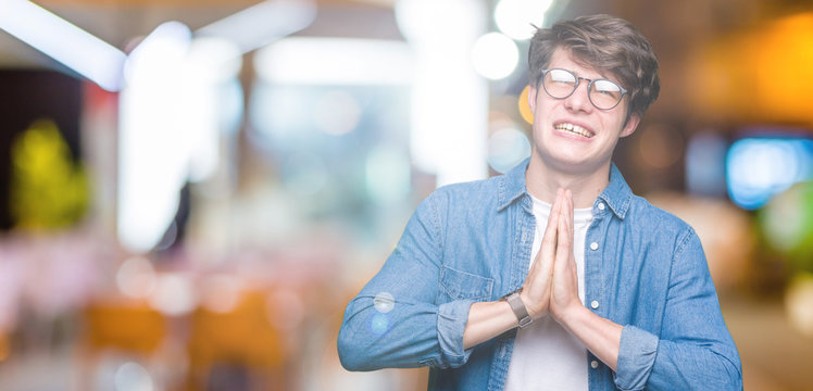 Young handsome man wearing glasses over isolated background begging and praying with hands together with hope expression on face very emotional and worried. Asking for forgiveness. Religion concept.