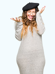 Fototapeta premium Beautiful young woman wearing glasses and fashion beret celebrating mad and crazy for success with arms raised and closed eyes screaming excited. Winner concept