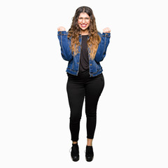 Young beautiful woman wearing glasses and denim jacket celebrating surprised and amazed for success with arms raised and open eyes. Winner concept.