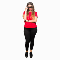 Young beautiful woman wearing red t-shirt and sunglasses skeptic and nervous, disapproving expression on face with crossed arms. Negative person.