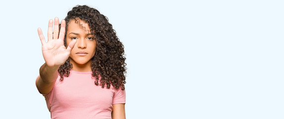 Young beautiful woman with curly hair wearing pink t-shirt doing stop sing with palm of the hand. Warning expression with negative and serious gesture on the face. - obrazy, fototapety, plakaty