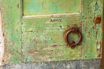 Detail of a green door with rusty iron ring.