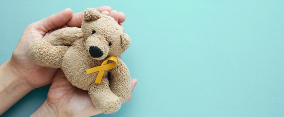 Hands holding children soft toy brown bear with yellow gold ribbon, Childhood cancer awareness