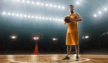 Young professional basketball player in sports uniform on a court with a ball. Floodlit sports arena