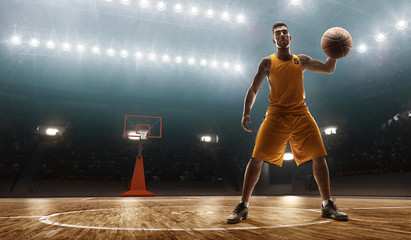 Young professional basketball player in sports uniform on a court with a ball. Floodlit sports arena