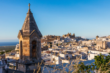 Italy, Apulia, Province of Brindisi, Ostuni. View over the town with unidentified church bell tower in foreground and Church of San Vito Martire on hill in background.