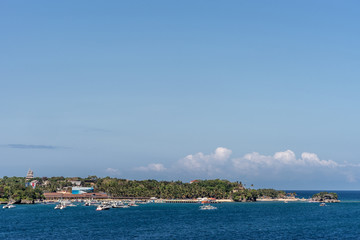 Manoc-Manoc, Boracay, Philippines - March 4, 2019: Wide shot from sea of Cagban Jetty Port with tens of small boats. Dark blue see in front, green band of jungle trees with some red roofs under blue s