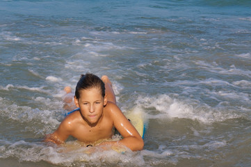 Boy surfing on yellow body board in blue sea