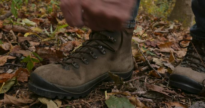 Hand held shot of a man lacing up and tying his hiking boots in the forest