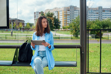 Happy woman uses a tablet or ebook on a tram station while waiting for public transport.