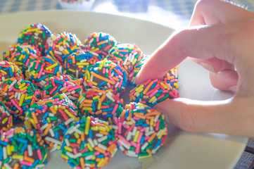 hand choosing typical brazilian sweet at birthday parties, Brigadeiro, with colorful chocolate sprinkles on white plate