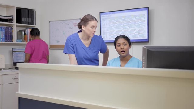 Three nurses at nursing station, two discuss as camera moves left then right