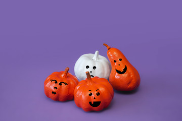 Pumpkins with  funny faces on violet background, creative concept. Festive advertising flat lay banner, front view. Decor for celebration. Modern trendy halloween composition with copy space