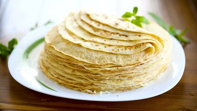 many fried thin pancakes in a plate, on a table.