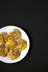 Homemade garlic thyme smashed potatoes on a white plate on a black surface, top view. Flat lay, overhead, from above. Copy space.