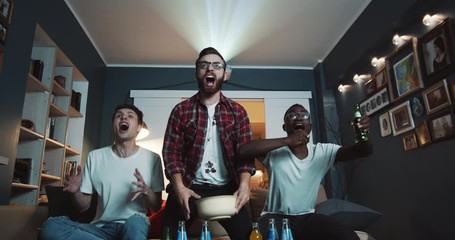 Happy diverse male sports fans celebrate goal and shout watching game together at home on big screen slow motion.