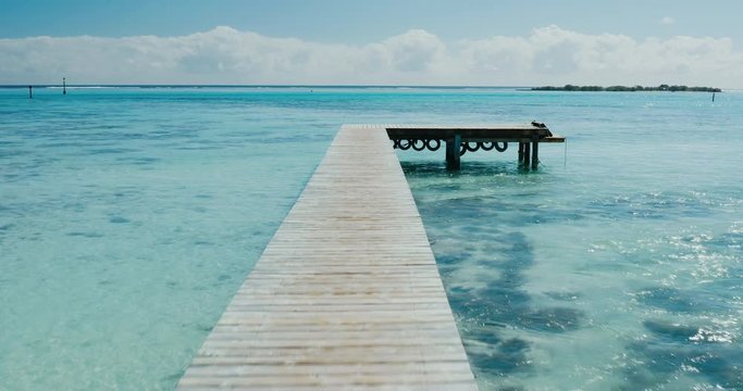 Aerial view flying over deserted wooden dock out towards calm blue ocean lagoon