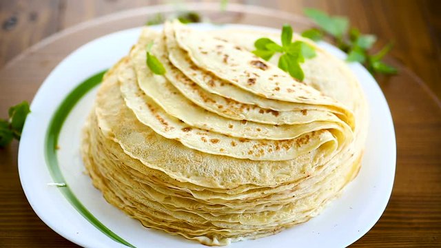 many fried thin pancakes in a plate, on a table.