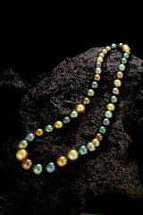 A necklace of a strand of multi colored round pearls on a dark stone background.