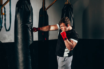 Muscular kickbox fighter exercising with punch bag at the gym