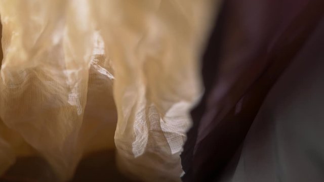 Translucent yellow chiffon curtain. Bedroom, cafe or club close-up back lit. Vertical fold. Sunlight shines through fabric. Macro shooting textile. Private atmosphere. Pan shot. Beautiful portieres.