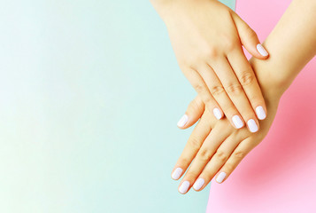 Female hands with white manicure on a pink and blue background, top view