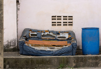 The old furniture was abandoned behind an old wall with a trash bin on the side.