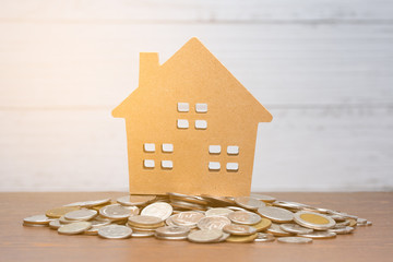 Model house put on many stack of coin on wooden table with white wood background and flare light effect,saving for buy house and real estate or loan for business investment concept