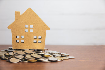 Model house put on many stack of coin on wooden table with white wood background and flare light effect,saving for buy house and real estate or loan for business investment concept
