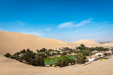 A distant man walking across the sand dunes, away from an oasis near Huacachina in the desert of Peru on a clear sunny day