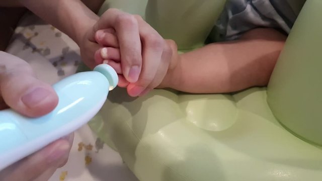 Mother is filling baby toe nails, difficult holding foot by her hand,using automatic file machine while baby movement is very convinience and easily triming by let's your baby take a seat.