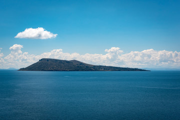 The picturesque hills of Moon Island protruding from the beautiful blue water of Lake Titicaca on a partially cloudy day