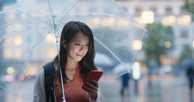 Woman hold with umbrella and use of mobile phone in the city at night