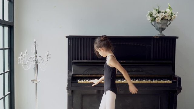 4K Tracking shot happy little child girl dancer in black leotard and ballet slipper shoes jumping and dancing contemporary ballet dance practice at vintage studio room. Young girl dancing in the room.