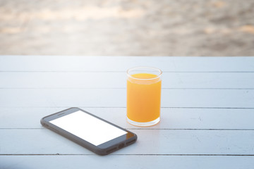 Orange juice in glass and mobile phone on white wooden table