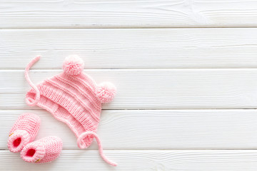 Fototapeta na wymiar Knitted pink footwear and hat for baby on white wooden background top view mockup