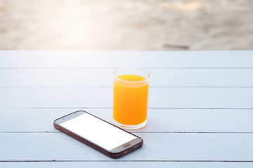 Orange juice in glass and mobile phone on white wooden table