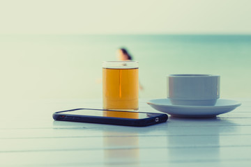 Tea coffee with smart phone on the white wooden table at the beach