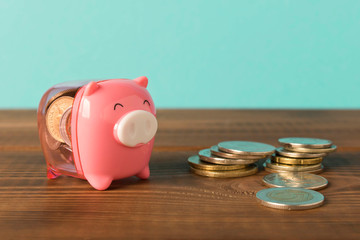 Little piggy Bank and a few coins on the wooden table. Close up. The concept of saving money.