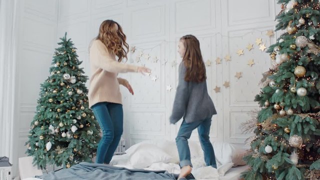 Cheerful mother and daughter having dance party on bed in luxury house.