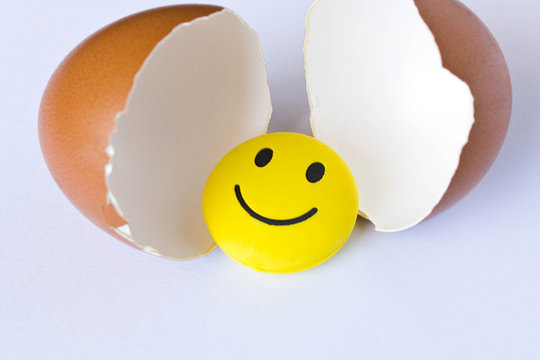 Funny yellow smiley toy in an egg-shell. On white background.