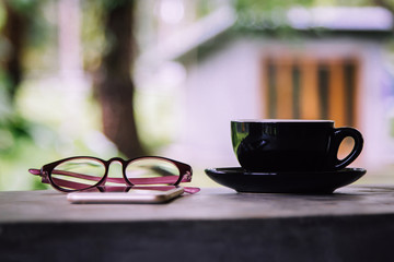 Coffee cup,smartphone and reading glasses on cement table with nature background