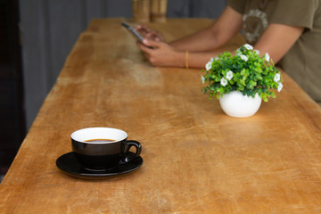 Coffee cup on an old wooden table with a woman using a smartphone